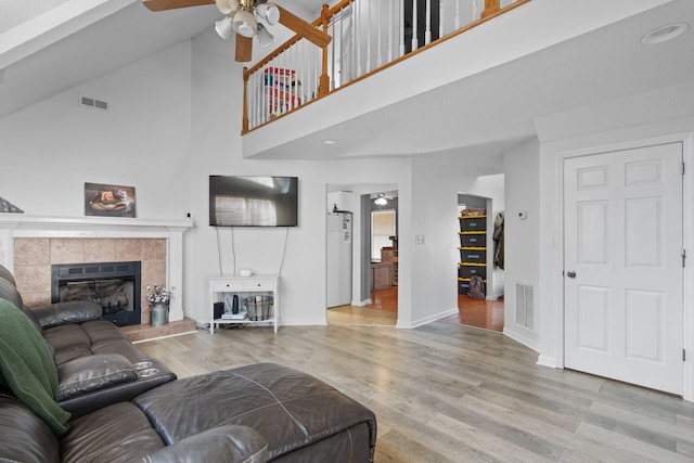 living room featuring a tiled fireplace, a towering ceiling, light hardwood / wood-style floors, and ceiling fan