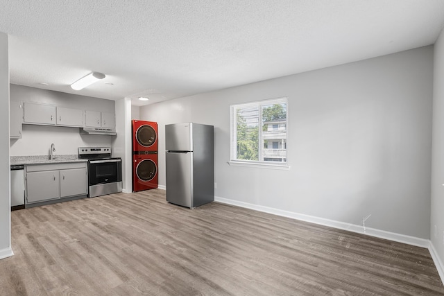 kitchen with stacked washer and dryer, sink, a textured ceiling, light wood-type flooring, and appliances with stainless steel finishes