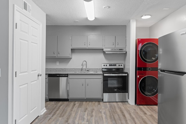 kitchen featuring sink, a textured ceiling, appliances with stainless steel finishes, gray cabinets, and stacked washer / dryer