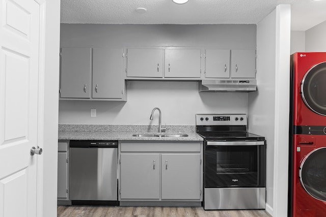 kitchen with stacked washer / dryer, appliances with stainless steel finishes, sink, and a textured ceiling