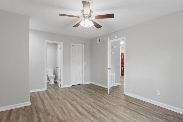 unfurnished bedroom with stacked washer and clothes dryer, connected bathroom, a closet, ceiling fan, and light hardwood / wood-style floors