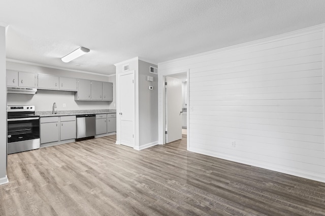 kitchen with appliances with stainless steel finishes, wooden walls, a textured ceiling, and gray cabinetry