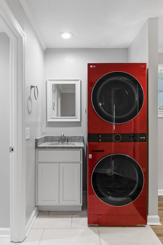 laundry room with sink, stacked washer and clothes dryer, ornamental molding, a textured ceiling, and light tile patterned flooring