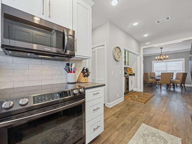 kitchen featuring pendant lighting, appliances with stainless steel finishes, white cabinets, decorative backsplash, and light wood-type flooring