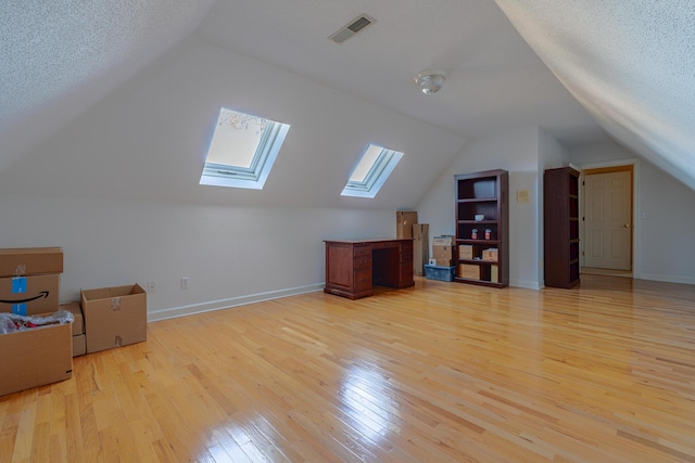 additional living space with vaulted ceiling, a textured ceiling, and light hardwood / wood-style flooring