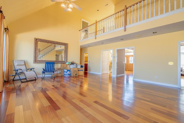 living room featuring ceiling fan, a towering ceiling, and wood-type flooring