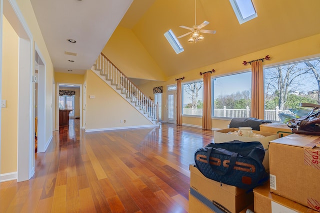 living room featuring hardwood / wood-style flooring, a skylight, high vaulted ceiling, and ceiling fan