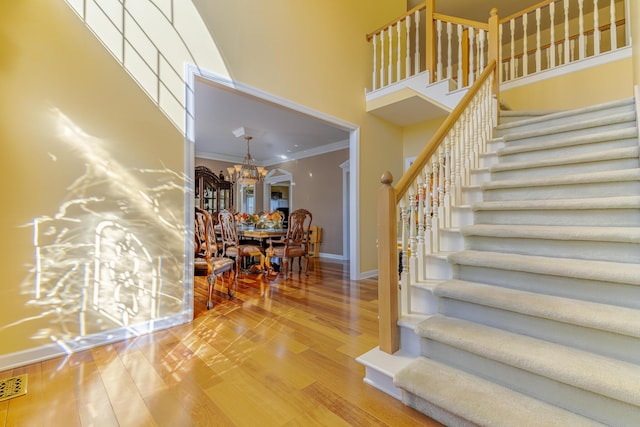 staircase with hardwood / wood-style flooring, ornamental molding, a chandelier, and a high ceiling