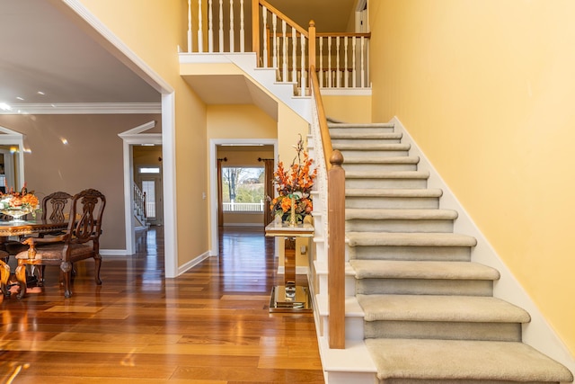 stairway featuring a towering ceiling, ornamental molding, and hardwood / wood-style floors