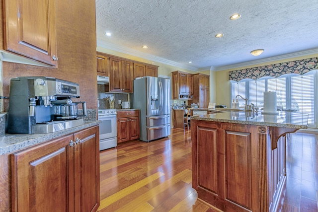 kitchen featuring hardwood / wood-style floors, ventilation hood, white gas range, stainless steel fridge, and a kitchen bar