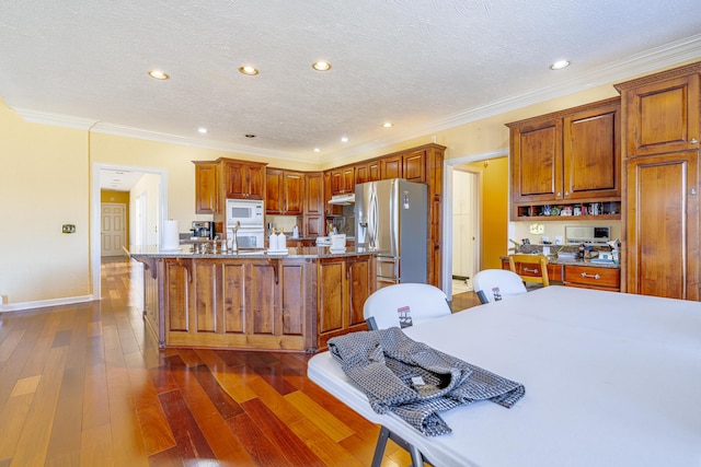 kitchen featuring a kitchen island with sink, white appliances, dark hardwood / wood-style flooring, and crown molding