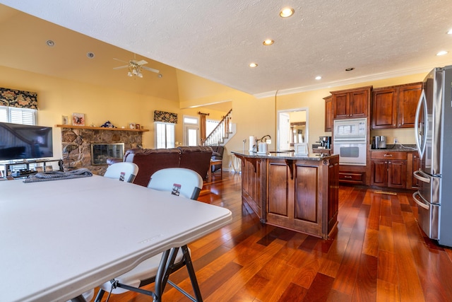 kitchen with a stone fireplace, a wealth of natural light, a kitchen bar, a center island with sink, and white appliances