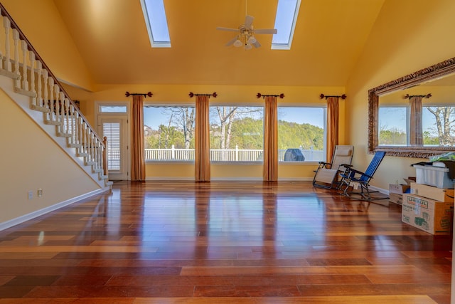 living room with ceiling fan, dark hardwood / wood-style flooring, a skylight, and high vaulted ceiling