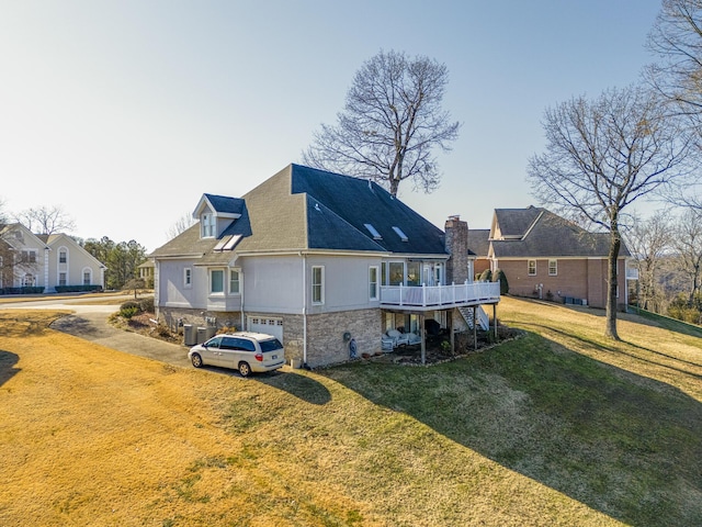 rear view of property featuring a wooden deck, a garage, and a lawn