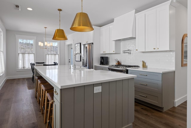 kitchen with pendant lighting, a breakfast bar area, premium range hood, stainless steel appliances, and a center island with sink