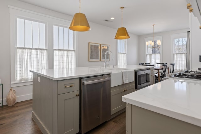 kitchen featuring gray cabinets, appliances with stainless steel finishes, dark hardwood / wood-style floors, pendant lighting, and a kitchen island with sink