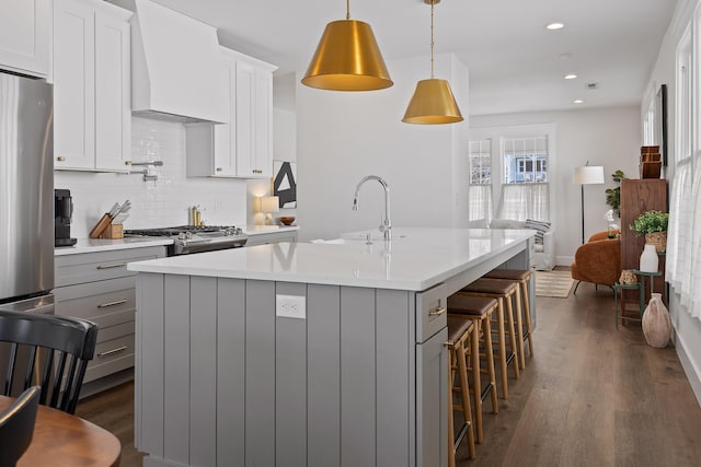 kitchen featuring custom exhaust hood, white cabinetry, an island with sink, pendant lighting, and backsplash