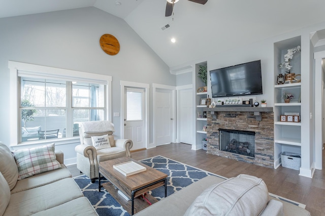 living room with built in shelves, wood-type flooring, a stone fireplace, and vaulted ceiling