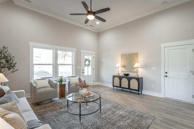 living room featuring a high ceiling, wood-type flooring, ornamental molding, and ceiling fan