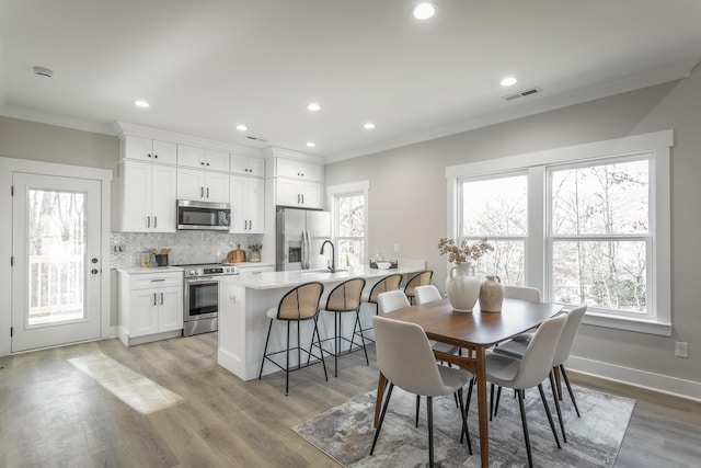 dining space with ornamental molding, sink, light hardwood / wood-style flooring, and a wealth of natural light