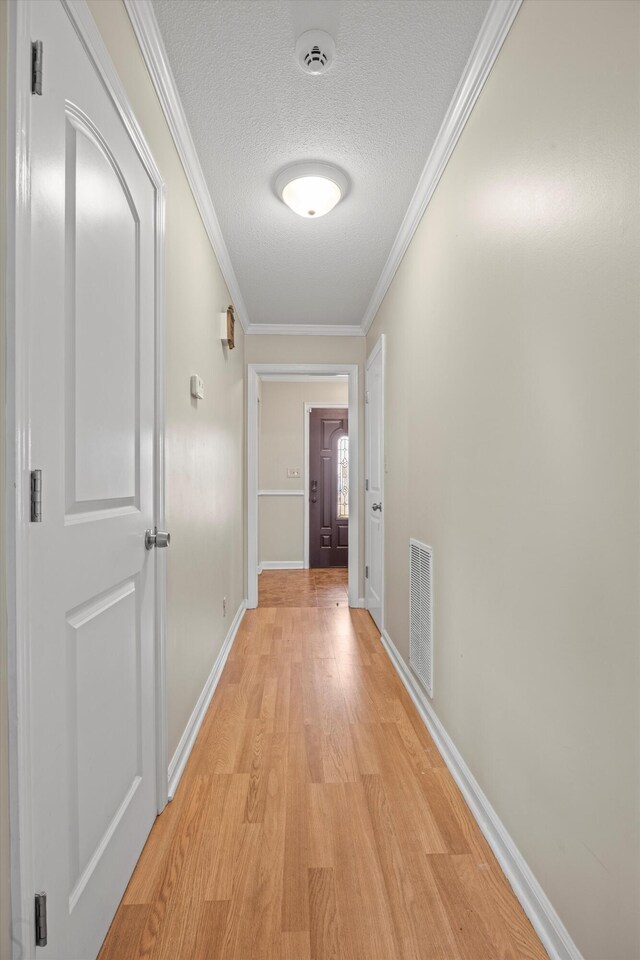 hall with baseboards, visible vents, a textured ceiling, crown molding, and light wood-style floors