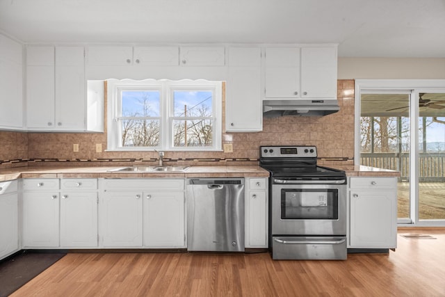 kitchen featuring white cabinets, light wood-style flooring, stainless steel appliances, under cabinet range hood, and a sink