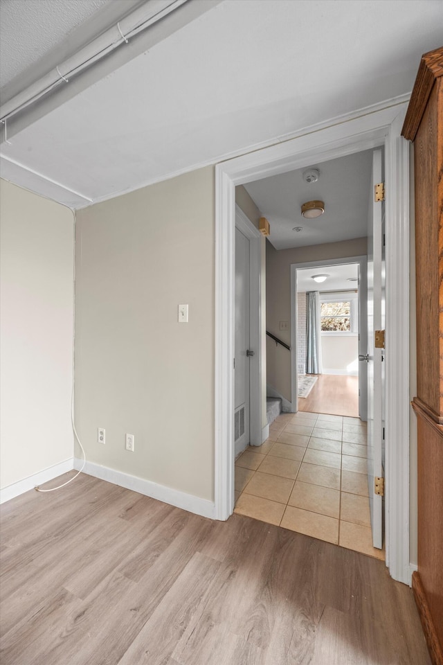 hallway with light wood-type flooring, visible vents, and baseboards