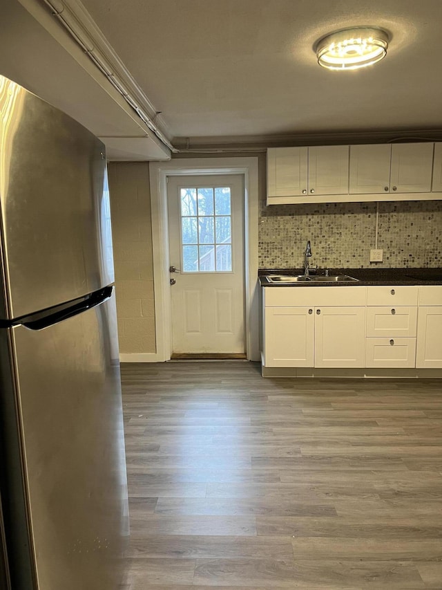 kitchen featuring light wood finished floors, dark countertops, freestanding refrigerator, white cabinetry, and a sink