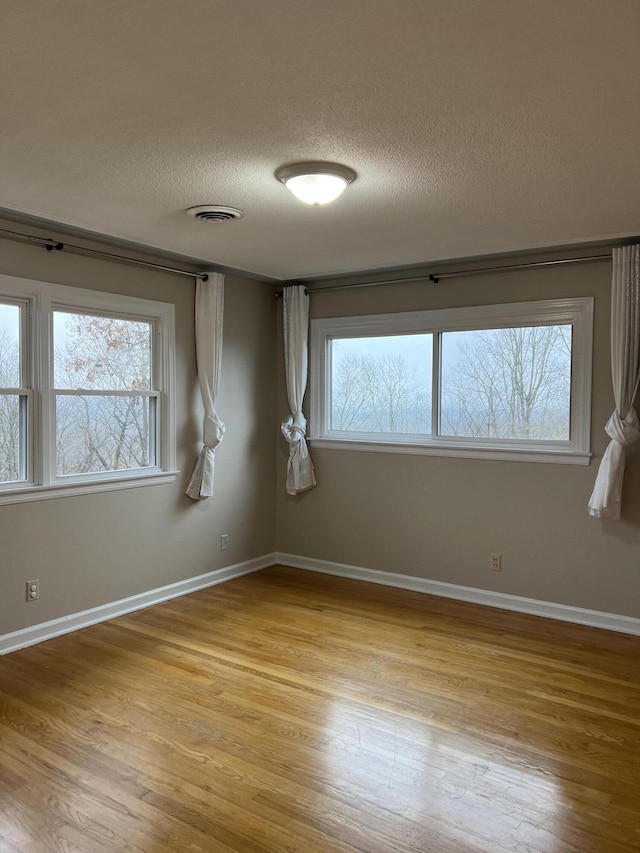 empty room with a textured ceiling, light wood-style flooring, plenty of natural light, and visible vents