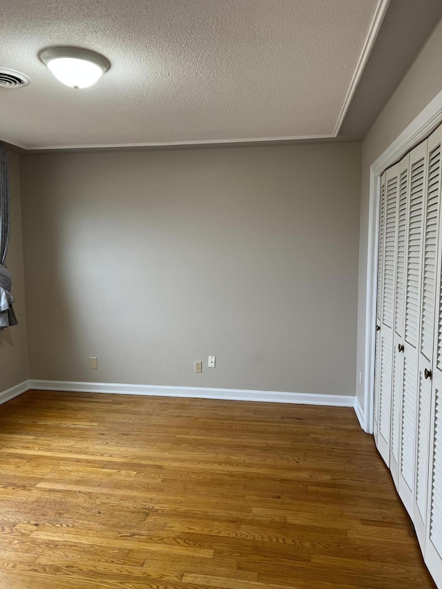 unfurnished bedroom with a textured ceiling, a closet, visible vents, and wood finished floors