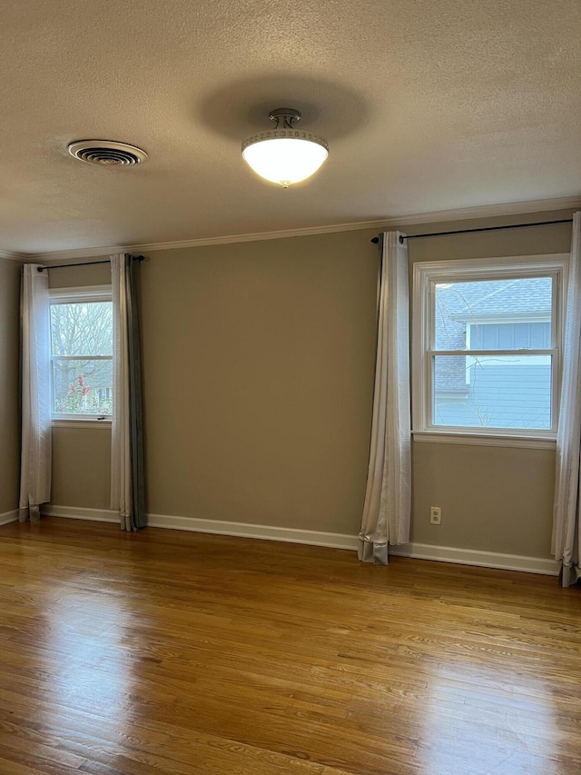 empty room featuring light wood-type flooring, visible vents, a textured ceiling, and baseboards