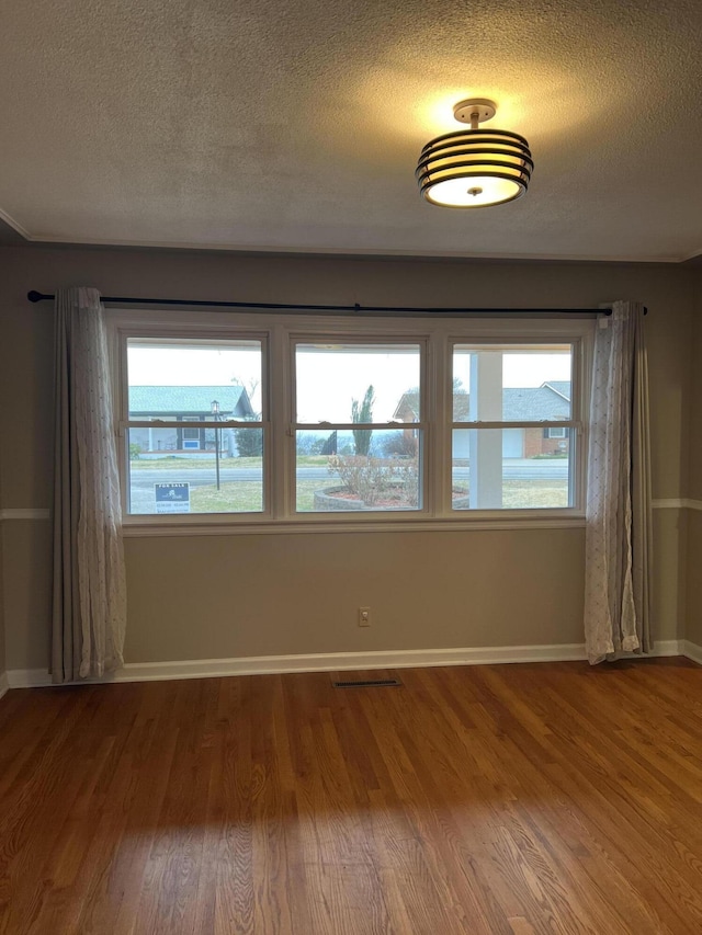 empty room with a healthy amount of sunlight, visible vents, and wood finished floors