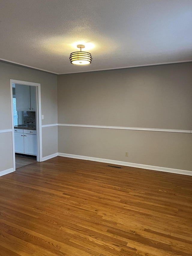 spare room with a textured ceiling, wood finished floors, visible vents, and baseboards