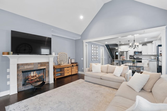 living room with high vaulted ceiling, a stone fireplace, an inviting chandelier, and dark hardwood / wood-style flooring