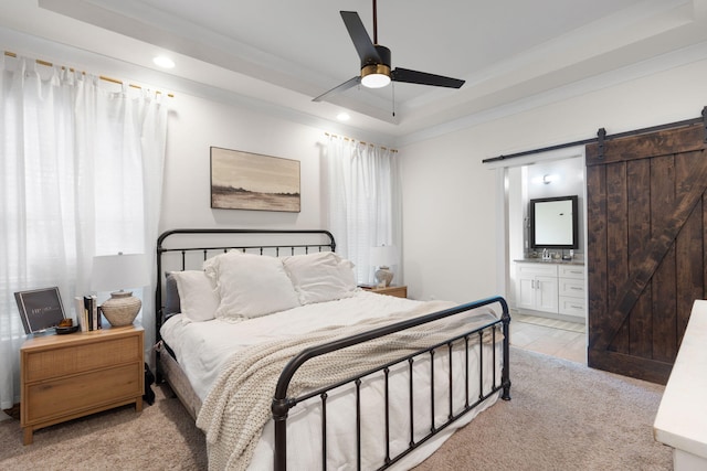 bedroom with ensuite bath, light colored carpet, a raised ceiling, ceiling fan, and a barn door