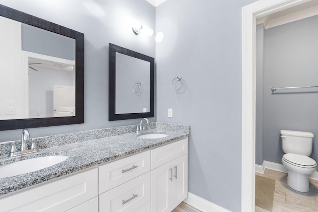 bathroom featuring baseboards, a sink, toilet, and double vanity