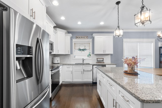 kitchen with decorative backsplash, white cabinets, appliances with stainless steel finishes, hanging light fixtures, and a sink