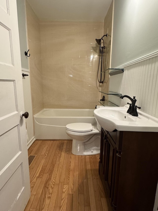 full bathroom with hardwood / wood-style flooring, tiled shower / bath, vanity, and toilet