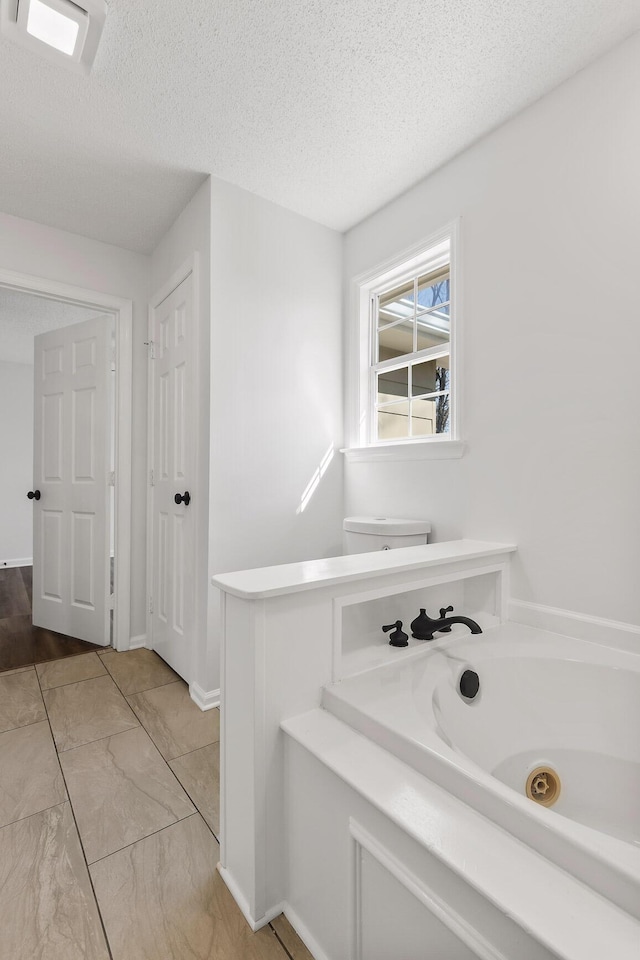 bathroom with a textured ceiling, toilet, and a bathing tub