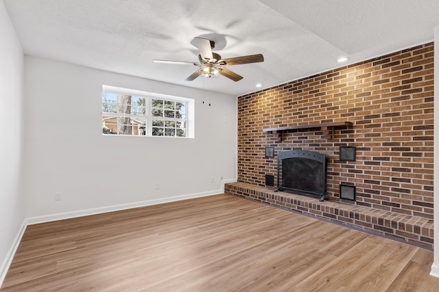 unfurnished living room featuring ceiling fan, a brick fireplace, a textured ceiling, and light wood-type flooring