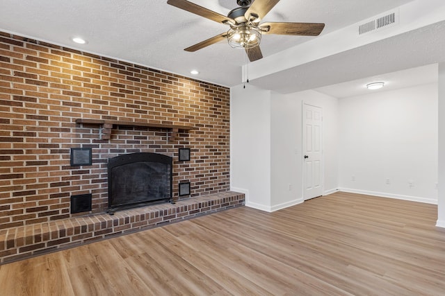 unfurnished living room with ceiling fan, a brick fireplace, a textured ceiling, and light wood-type flooring