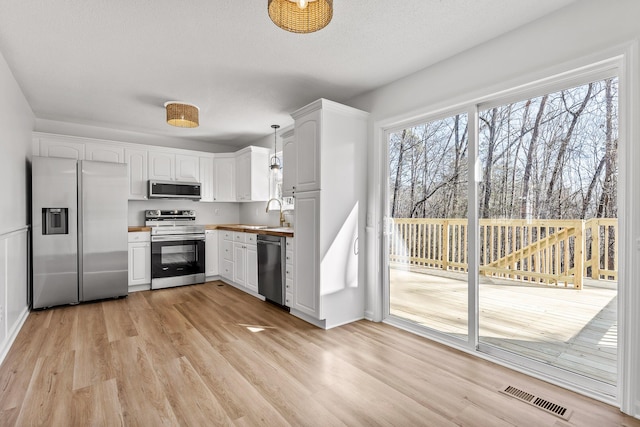 kitchen featuring light hardwood / wood-style flooring, hanging light fixtures, plenty of natural light, stainless steel appliances, and white cabinets