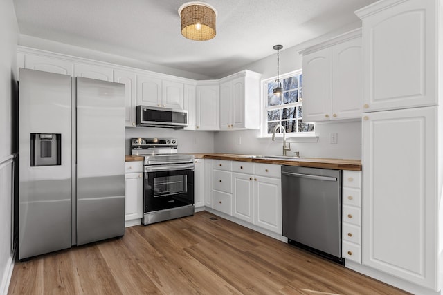 kitchen featuring pendant lighting, appliances with stainless steel finishes, butcher block countertops, and white cabinets