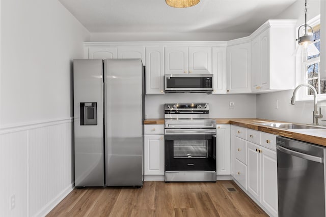 kitchen with stainless steel appliances, butcher block counters, white cabinets, and decorative light fixtures