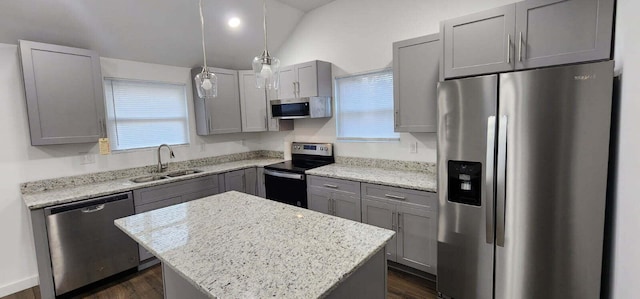 kitchen featuring sink, appliances with stainless steel finishes, a kitchen island, pendant lighting, and light stone countertops