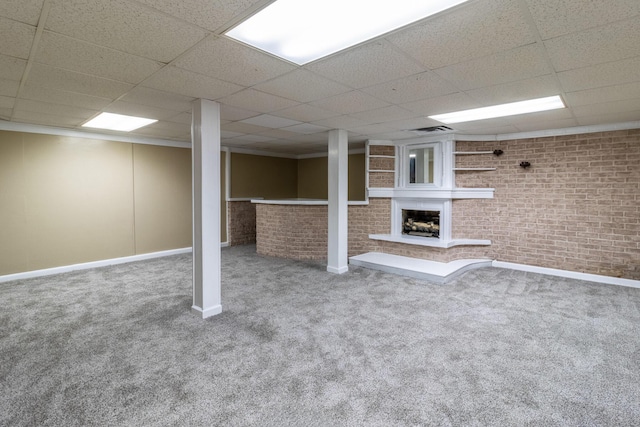 basement featuring carpet flooring, a fireplace, a paneled ceiling, and brick wall