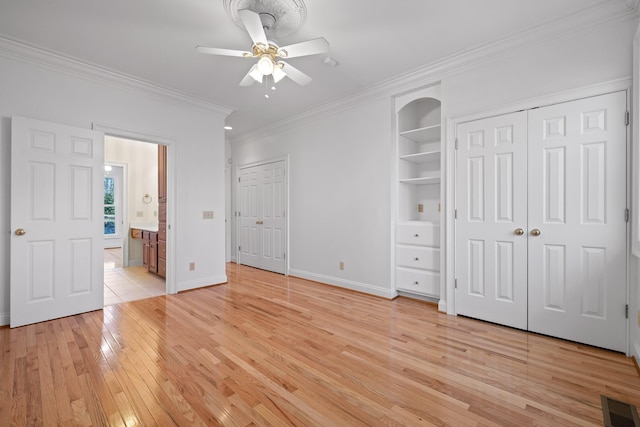 unfurnished bedroom featuring crown molding, multiple closets, visible vents, light wood-style floors, and baseboards