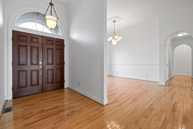 foyer entrance featuring arched walkways, a notable chandelier, visible vents, ornamental molding, and light wood-type flooring