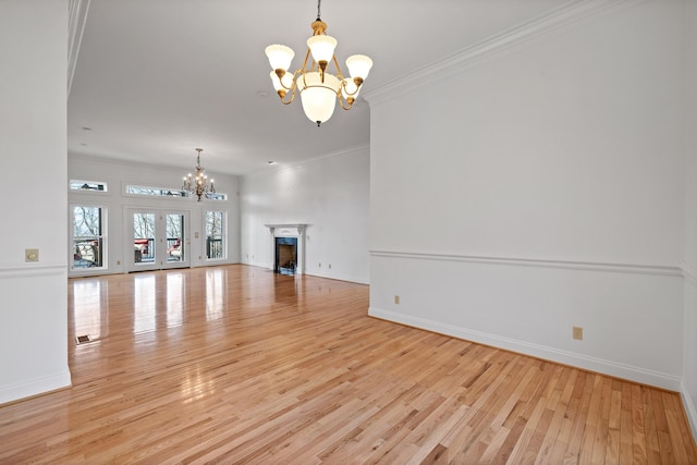 unfurnished living room with baseboards, ornamental molding, light wood-style floors, a fireplace, and a notable chandelier