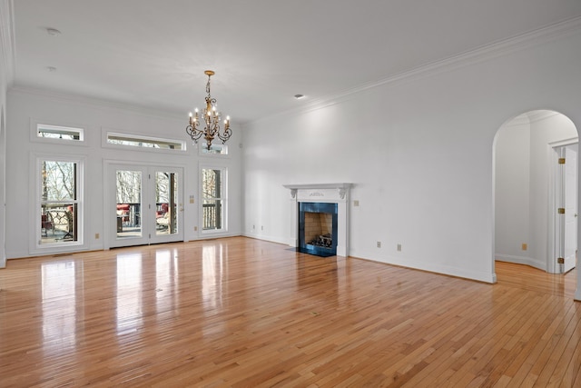 unfurnished living room featuring arched walkways, a fireplace with flush hearth, baseboards, light wood finished floors, and crown molding